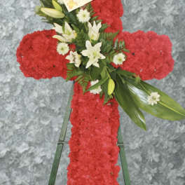 Red floral cross on a stand with white lilies and greenery