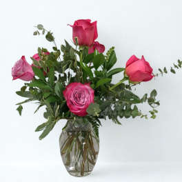 Pink roses arranged in a clear glass vase with greenery