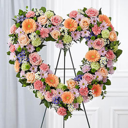 Heart-shaped floral wreath on a black stand with pink, peach, and orange blooms