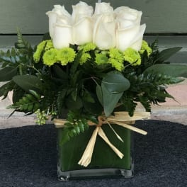 White roses and green mums in a square glass vase with a raffia bow