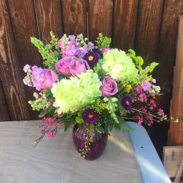 Bouquet of pink roses, green hydrangeas, and purple accent flowers in a glass vase