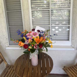 Colorful mixed flower bouquet in a pink vase on a patio table