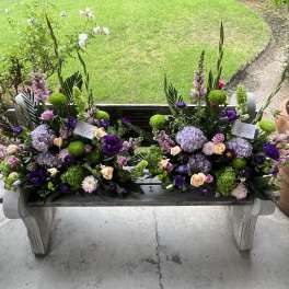 Two floral arrangements on a bench in purple, green, and peach tones