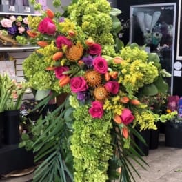 Tall cross-shaped standing spray with green hydrangeas, hot pink roses, and orange blooms on a metal easel