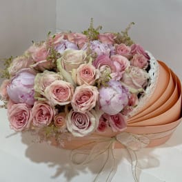 Bouquet of pale pink roses and peonies in a peach hatbox