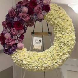 Large crescent floral wreath on an easel with purple, pink, and cream flowers