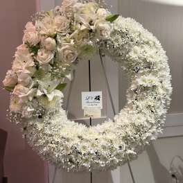 Large white floral wreath on a stand with pale pink roses and lilies