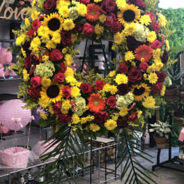 Large floral wreath with red roses, yellow blooms, and sunflowers on a stand