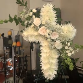 White floral cross arrangement on a stand with pale pink roses