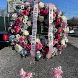 Large floral standing wreath with pink and white flowers and memorial ribbons