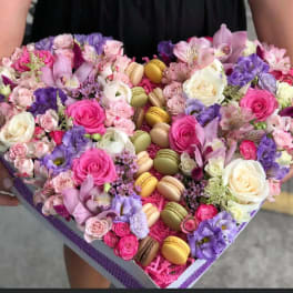 Heart-shaped box of pink and purple flowers with macarons