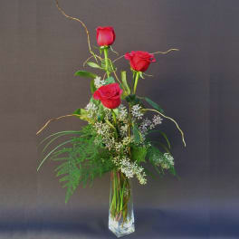 Tall vase arrangement with three red roses and white filler flowers