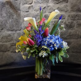 Colorful bouquet with calla lilies, tulips, and blue hydrangeas in a glass vase
