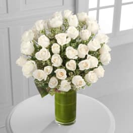 White roses arranged in a tall green glass vase