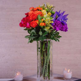 Colorful bouquet in a tall glass vase with candles on either side