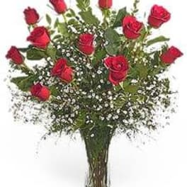Tall arrangement of long-stem red roses with white filler flowers in a clear glass vase