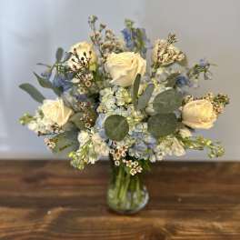Arrangement of cream roses, blue hydrangeas, and small white flowers in a clear glass vase
