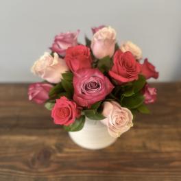 Compact arrangement of pink and lavender roses in a white vase on a wooden surface