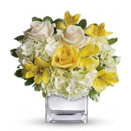 Yellow and white floral arrangement in a clear square vase