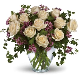Arrangement of cream roses and small purple flowers in a clear glass vase