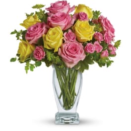 Arrangement of pink and yellow roses and spray roses in a clear glass vase