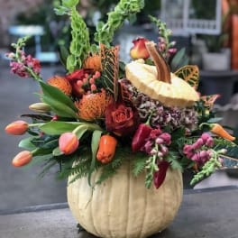 Autumn floral arrangement in a pumpkin-shaped container with roses and tulips