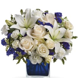 White roses and lilies arranged in a blue glass vase