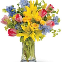 Vase arrangement of yellow lilies and roses with pink tulips and blue delphinium