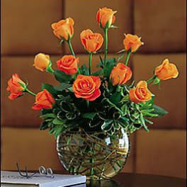 Low arrangement of orange roses in a round glass vase on a table