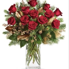 Red roses arranged in a clear glass vase with evergreen accents