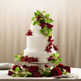 Three-tier white cake decorated with green orchids and red roses on a pedestal stand