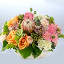 Mixed bouquet of peach, pink, and white flowers in a low white container