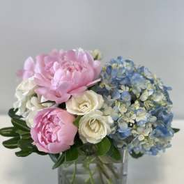 Pink peonies, white roses, and blue hydrangeas in a square glass vase