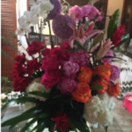 Tall mixed arrangement with red and pink roses, orange flowers, lilies, orchids, and white blooms.
