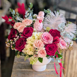 Pink and red rose arrangement in a white vase with a small poodle figurine