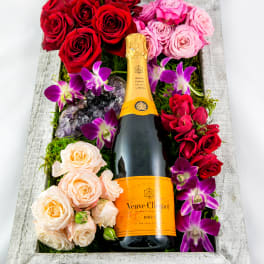 Champagne bottle surrounded by red, pink, and peach roses in a wooden box