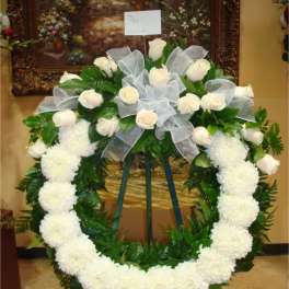 White rose and chrysanthemum funeral wreath on an easel with a ribbon bow