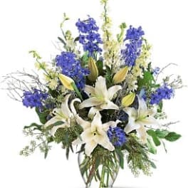 Tall arrangement of white lilies and blue flowers in a clear glass vase