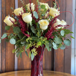 Cream roses in a tall red vase with burgundy accents