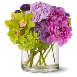 Compact arrangement of pink and purple flowers with green orchids in a clear glass cylinder vase