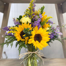 Bouquet of sunflowers, purple flowers, and yellow blooms in a glass vase