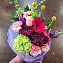 Bouquet of pink, purple, and green flowers wrapped in lavender paper