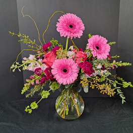 Pink gerbera daisies and mixed blooms in a clear glass vase