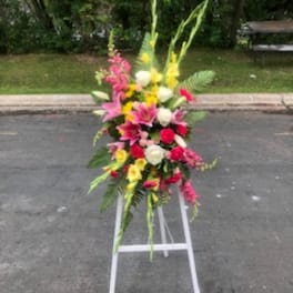 Tall standing floral spray with pink, yellow, and white flowers on a white easel