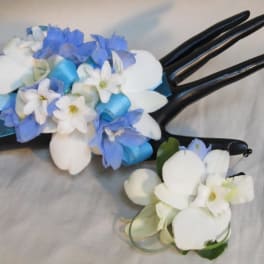 Two small floral corsages with blue and white flowers on black display hands.