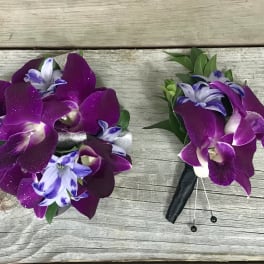 Two purple orchid boutonnieres on a wooden surface