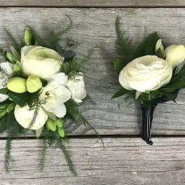 White floral boutonniere and matching wrist corsage on a wood surface