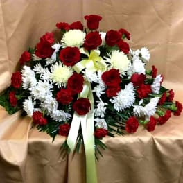 Red roses and white chrysanthemums arranged with a pale ribbon on tan fabric