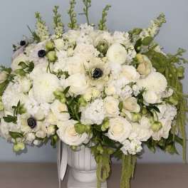 White floral arrangement in a white urn vase with trailing green accents