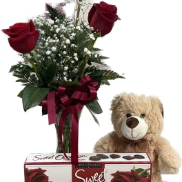 Red roses in a vase with a teddy bear and chocolate box